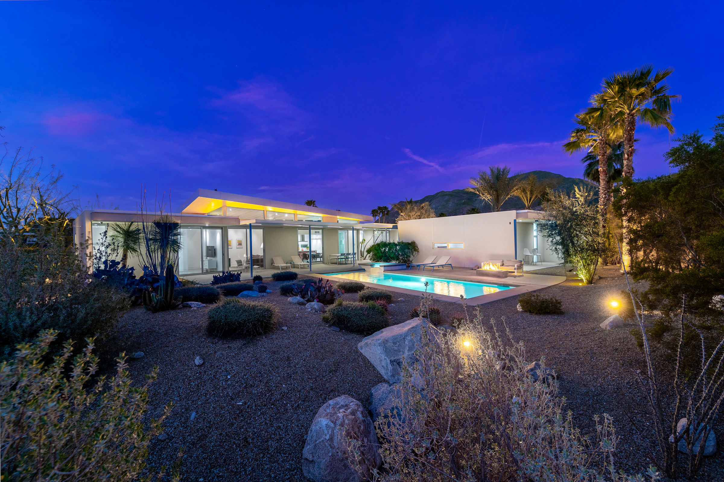 Modern desert villa with palm trees and pool at blue hour